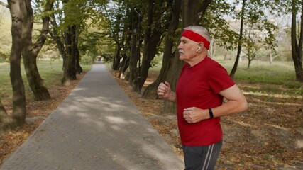 Obraz premium Side view of elderly sport runner man training. Workout cardio outside in city park at morning