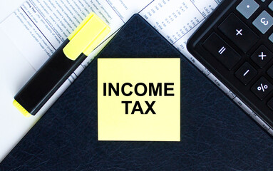Yellow sticker with text Income Tax laying on the folder with yellow marker and calculator