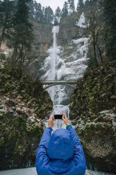 Woman using mobile device to take picture of waterfall.