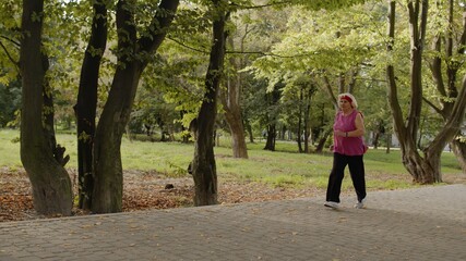 Senior old woman running in park and using smart watch. Female runner working out cardio outdoor