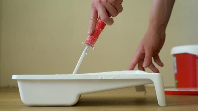 Close-up shot of a roller picking up paint from a plastic tub. Footage. Home renovation and renovation concept.