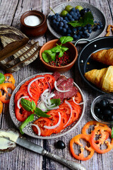Vertical composition of sliced tomatoes and salami, grapes, croissants on a rustic background. Top view