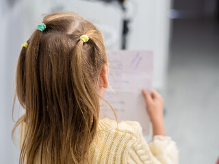 Fototapeta premium Little girls with blond hair are reading a note on a sheet. Back view. Girl in yellow sweater