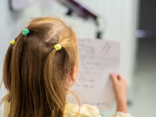 Naklejka premium Little girls with blond hair are reading a note on a sheet. Back view. Girl in a yellow sweater