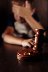 Divorce and alimony concept. Wooden gavel, rings and frustrated boy with teddy bear