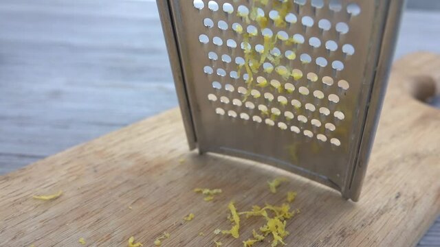 Close-up of lemon grating on the metal grater into the lemon zest in slow motion