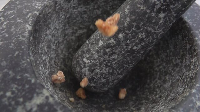 Pieces of brown sugar are falling into the grey stone mortar in slow motion