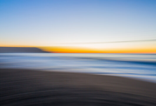 Motion blur of waves and cliff on a beach at sunset