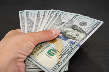 close-up of one hundred dollar bills in a female hand on a black wooden background.