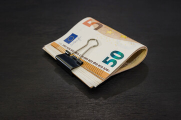 Bundle of 50 euro banknotes sealed with a clip on a black wooden background