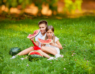 Naklejka na ściany i meble boy and girl sit on the grass and eat watermelon