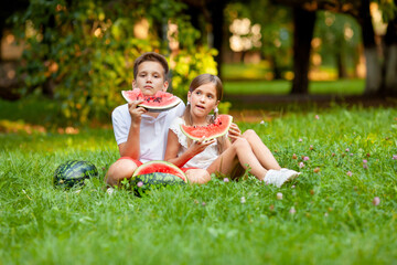 boy and girl sit on the grass and eat watermelon