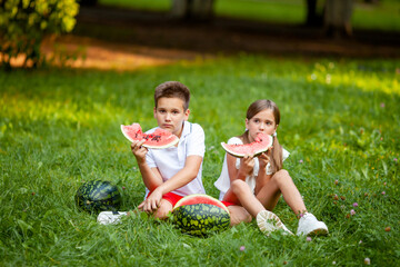Naklejka na ściany i meble boy and girl sit on the grass and eat watermelon