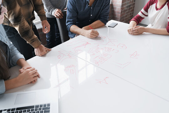Torso and arms of group using table top as white board in meetin