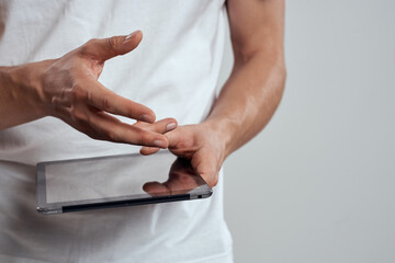 Tablet with a touch screen on a light background male hands white t-shirt cropped view