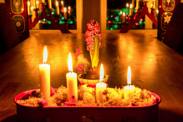 Burning Advent candles, red candlestick, oak table, close view Christmas Eve. Traditional decoration in Swedish house with window lights, hyacinth flower with Santa Claus. Exclusive Greeting Card.