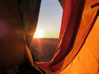 Orange touristic camping tent window looking on sun in sunrise. Recreation in nature romantic