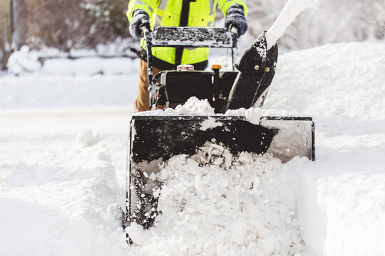 Man in vibrant yellow shirt using a snow blower to remove large amounts of snow