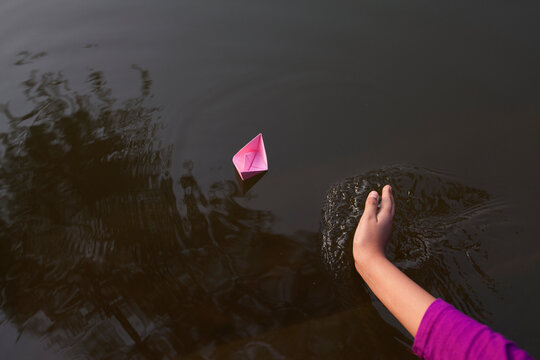 Teenage girl pusing water to asist of floating paper made boat on water