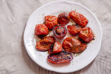 Old porcelain plate with roasted tomatoes isolated on beige tablecloth.
