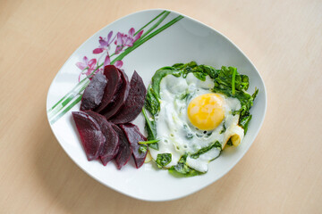 Fried egg with spinach and cooked beetroot on the dish. Healthy breakfast.