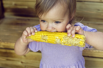 Little blonde girl eating corn of wooden background