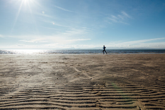 A man sprinting on a sandy beach on a sunny day, there are deep ripples in the sand