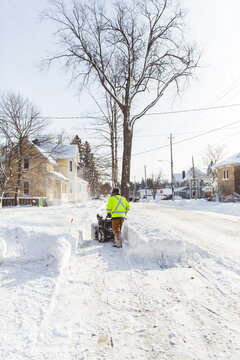 Man in vibrant yellow shirt using a snow blower to remove large amounts of snow