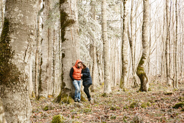 Obraz premium a couple, a man and a woman stand near a tree in a mountain forest in winter. honeymoon. walking and traveling.