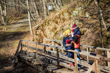 family with young daughters on a bridge in a mountain forest in winter in Sunny weather. traveling with children.