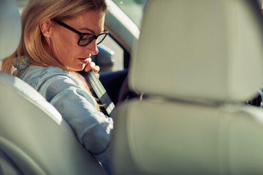 Rear View Of A Middle Aged Caucasian Woman, Business Lady Sitting Behind Steering Wheel Of Her Car And Fastening Seat Belt