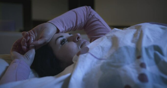 Sad pensive woman with an apathetic look lying on the bed and looking at the ceiling. Sleep problems, insomnia, thinking about her problems, can not sleep. Restless thoughts at night. 
