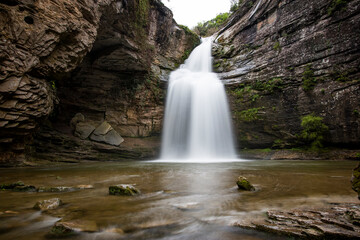 Fototapeta na wymiar Beautiful place with a waterfall that falls from the rocks of the mountain with the smooth water in long exposure. Tourism in Spain, Catalonia, Barcelona, Osona, Cantonigros, La Foradada.