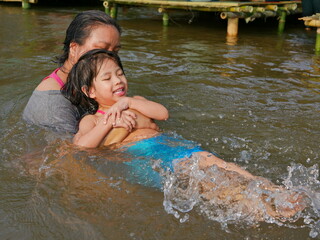Little baby girl enjoys playing water in a river with her auntie - playing outdoor and engaging with nature provides positive impact on children's health and development