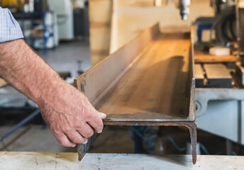 worker in a factory holds two metal beams before drilling holes in them