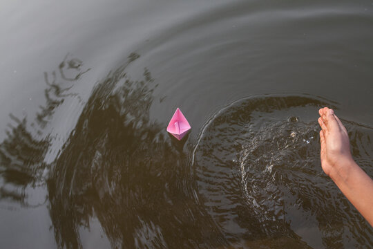 Teenage girl pusing water to asist of floating paper made boat on water