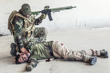 Army soldier, special forces fighter in ammunition, armed assault rifle, kneeling and placing two...