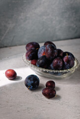 Red plums with water drops in a glass bowl on grey rustic background