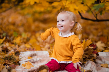 Adorable happy little girl in burgundy pants and a yellow jacket sits on a blanket near yellow...