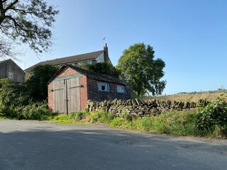 Old red brick garage, with a broken window, next to a dry stone wall, on Rishworth New Road, Ripponden, Sowerby Bridge, UK