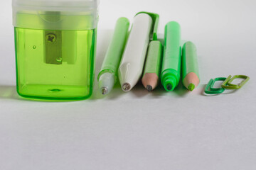 View directly on a green pencil, pen, felt-tip pen, sharpener, paper clips on a white table. Copy space.