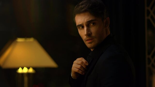 Top manager straightening shirt in dark room. Attractive man looking around.