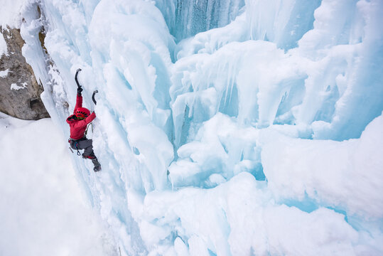 Female ice climber ascending on frozen waterfall