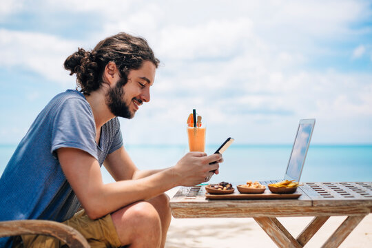 Man using laptop and phone on beach