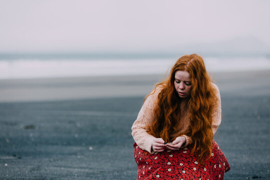 A beach comber crouching in the sand as she examines some sea-glass she has found on a beach in Scotland