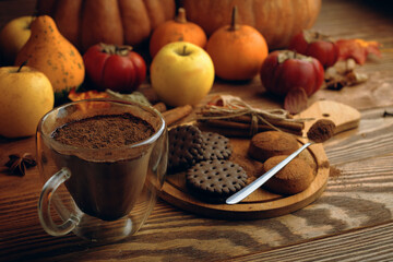 Hot cocoa, cookies and autumn harvest on wooden table. Ripe pumpkins, apples, fall leaves and persimmons on background. Coffee with chocolate chips. Concept of Christmas, Thanksgiving and Halloween.
