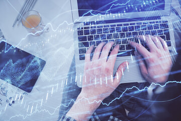 Double exposure of man's hands typing over laptop keyboard and forex chart hologram drawing. Top view. Financial markets concept.