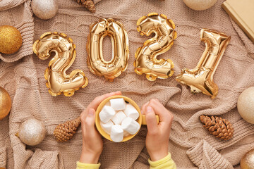 Figure 2020 made of balloons and female hands with cup of hot cacao on fabric background