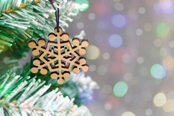 Close-up of a wooden snowflake hanging from a fir branch against a bokeh background. Simple christmas composition with free space, holiday background, postcard mockup, ecological toys