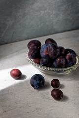 Red plums in a glass bowl on grey rustic background